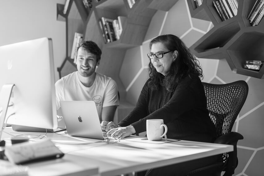 a man and a woman sitting at a table with a laptop.